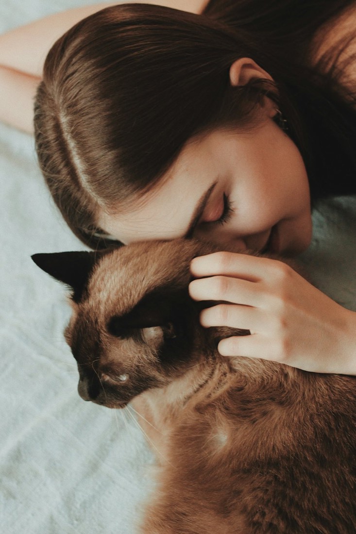 Une jeune femme pose sa tête contre son chat siamois