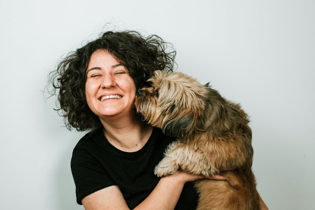 Un chien à poils longs fait un bisou à une femme qui rit