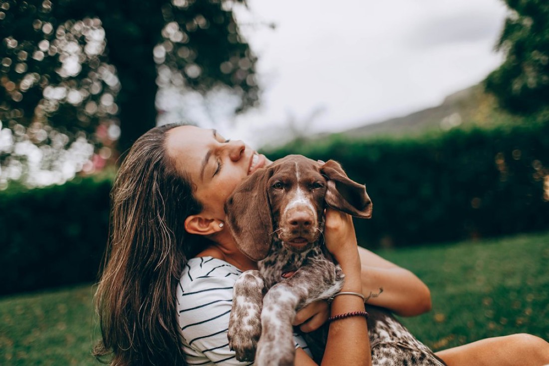 Une jeune femme serre un chiot braque contre elle dans l'herbe